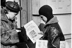 Photo title: "Newsboy distributing January 1937 Minneapolis Journal newspaper." Locator Number: M.18.A.1 Packet 7. Image depicts a boy in a leather jacket and hat. He has a bundle of newspapers in his hand and he is handing one to a woman. The woman appears to be looking in her purse for money.