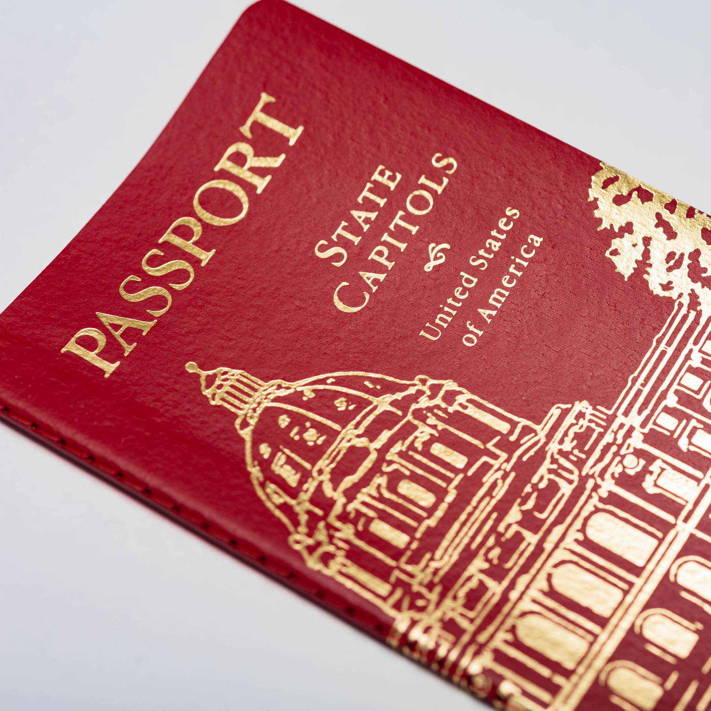 A close-up of the State Capitol Passport—a red booklet titled "Passport State Capitols United States of America," featuring a gold illustration of a capitol building on the cover—perfect for anyone ready to begin their state capitol passport journey and document their travels to each state capitol.