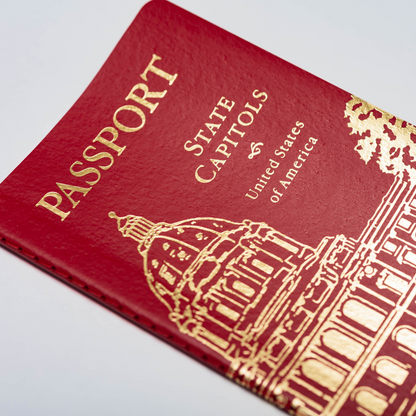 A close-up of the State Capitol Passport—a red booklet titled "Passport State Capitols United States of America," featuring a gold illustration of a capitol building on the cover—perfect for anyone ready to begin their state capitol passport journey and document their travels to each state capitol.