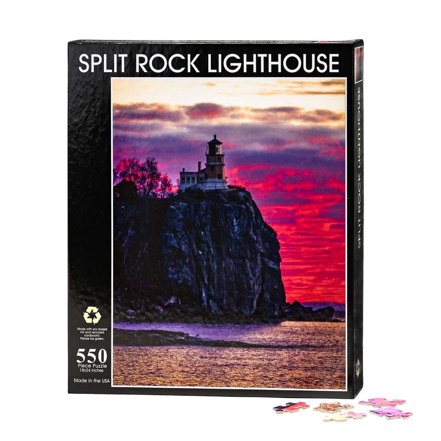 The Split Rock Sunrise by Stephanie Irwin Custom 550 piece puzzle box displays Irwin’s vibrant artwork of Split Rock Lighthouse atop a cliff at sunrise, with vivid pink, purple, and orange hues illuminating the sky above glistening water. Several loose puzzle pieces are arranged in front of the box.