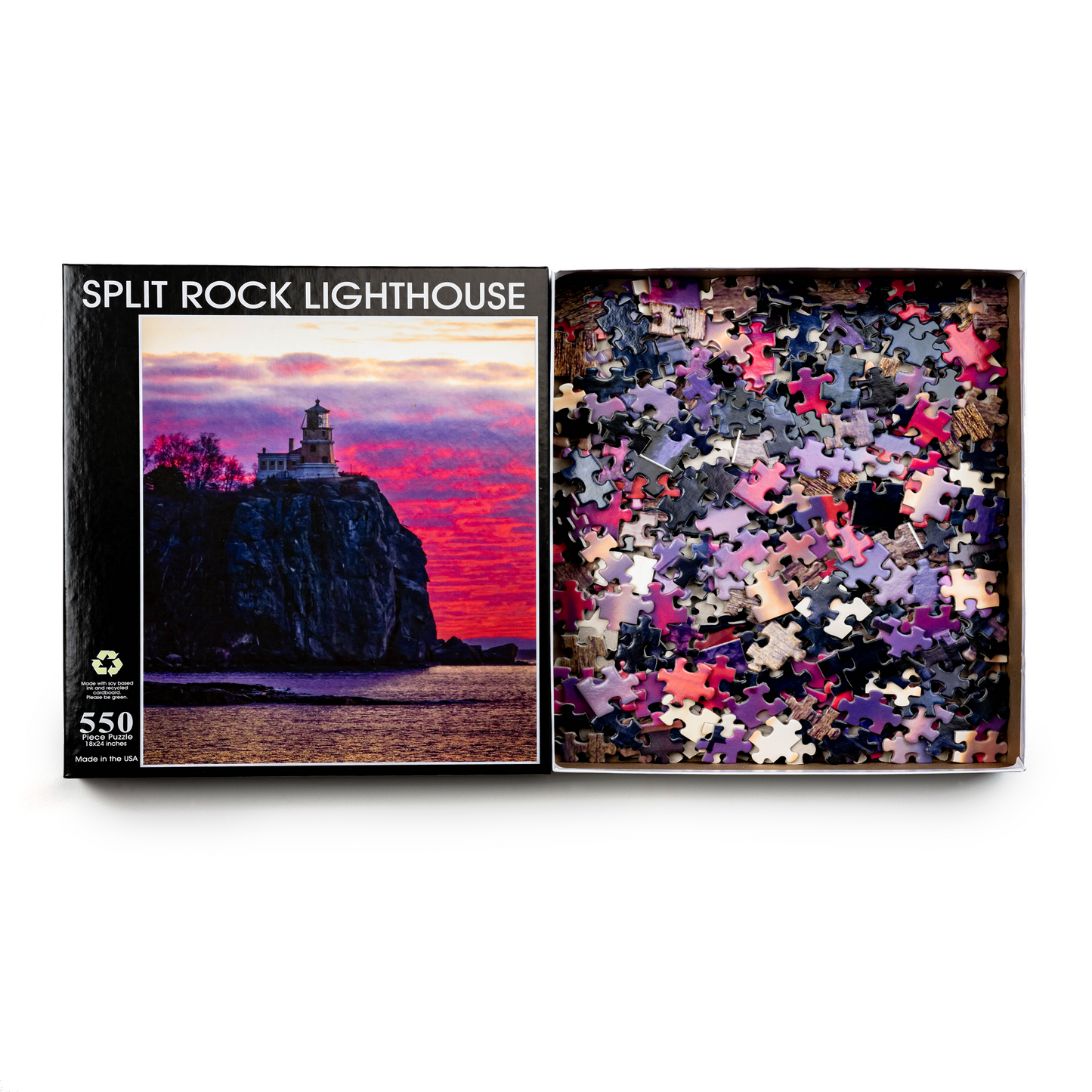 A box of the Split Rock Sunrise by Stephanie Irwin Custom 550 piece puzzle is open, displaying unsorted pieces whose colors reflect the vivid sunrise and iconic image of the lighthouse perched on a cliff, as depicted in Stephanie Irwin's design.