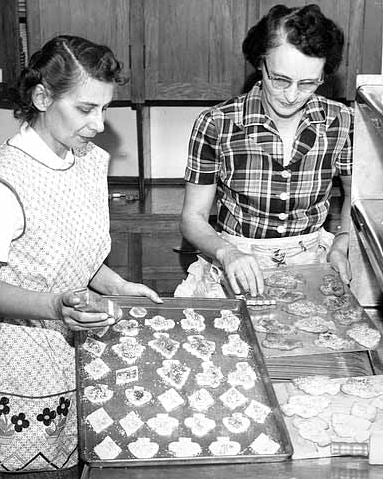 Same picture as previous, but it shows more of the scene and the two women's faces. Citation: Jacqueline Heinichs and Mrs. Joe LaVasseur making cookies for St. Louis HOme and School Association bake sale to raise money for Christmas for the school children.
Location #: GT4.8 p39
