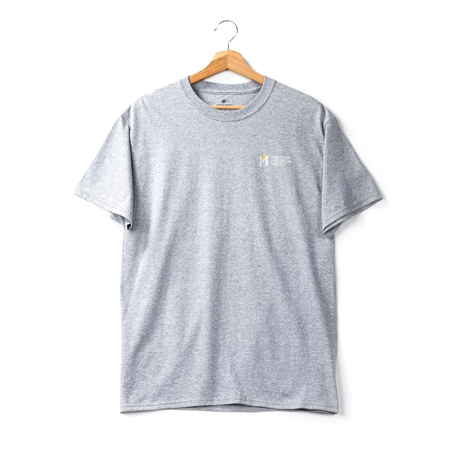 The Minnesota Historical Society Icon T-Shirt hangs on a wooden hanger against a white background, featuring a classic logo and text on the left chest.
