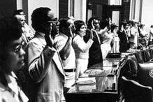 Men and women hold their right hands up as they take part in a naturalization ceremony, 1976. Title: "Naturalization ceremony for 113 new U.S. citizens. Citizenship Day, State Capitol. 1976. Photo locator: J4.8 p4 in the MNHS Collections.