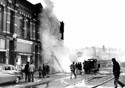 A group watches firefighters battle a smoky fire in a city building as hoses and a truck are visible. Smoke fills the scene with onlookers nearby. From MNHS collections. Order Image and Use via the MNHS Staff Image and Use Order Form.