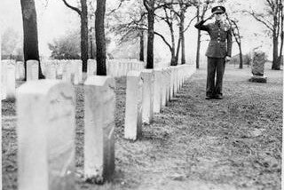 A soldier stands to attention and salutes a row of graves at Fort Snelling Cemetery. Title: "Burial plot of Unknown Soldiers, Fort Snelling National Cemetery. Photo locator:   MH5.9 F1.3CE p4 in the MNHS Collections.